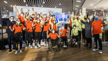 Das Team Deutschland Paralympics jubelnd am Flughafen in Frankfurt, Bundespräsident Steinmeier ist auf einem Bildschirm zu sehen